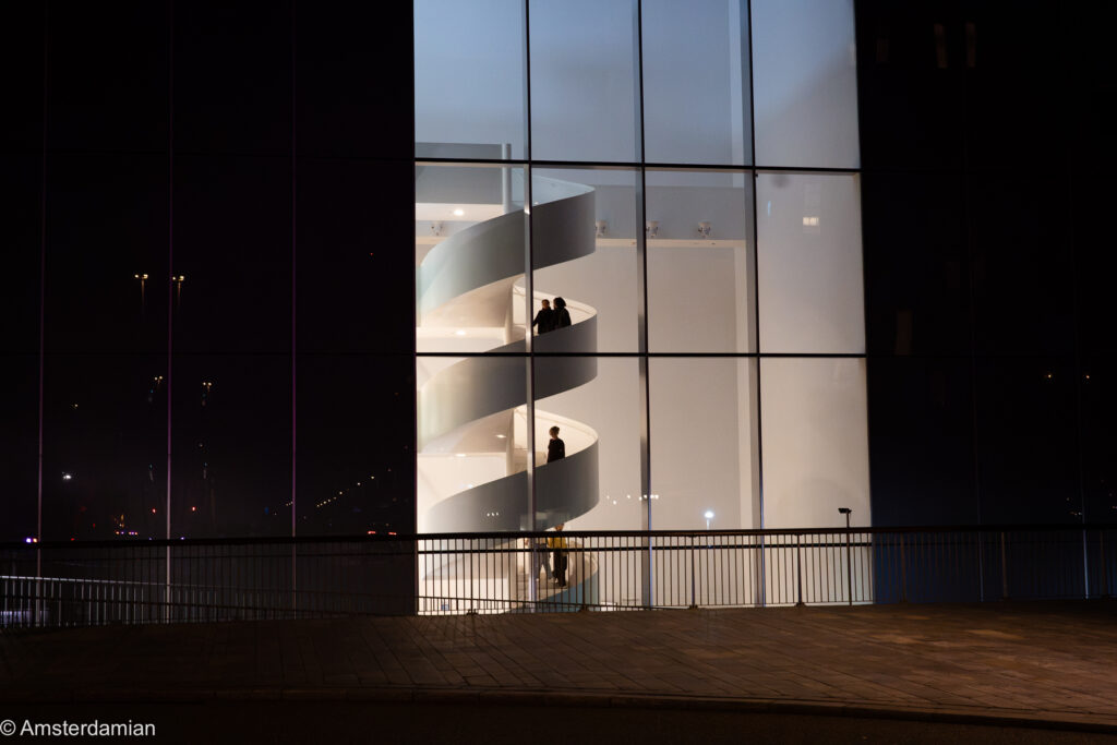 Lit-up spiral staircase behind the glass façade of KAF in Almere at night