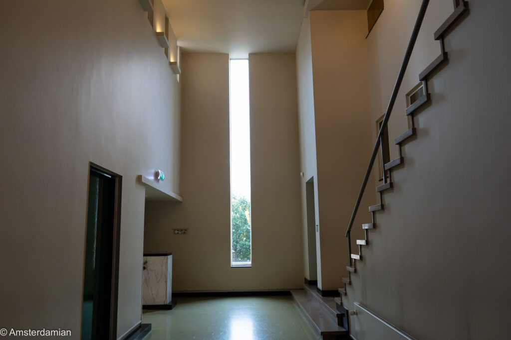 Stairwell with a tall narrow window inside Dudok's town hall