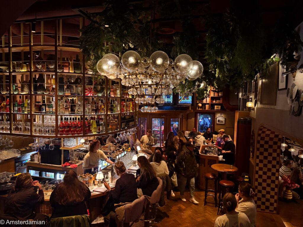 Busy bar with globe lamps and hanging plants at Gio Dio in Hilversum